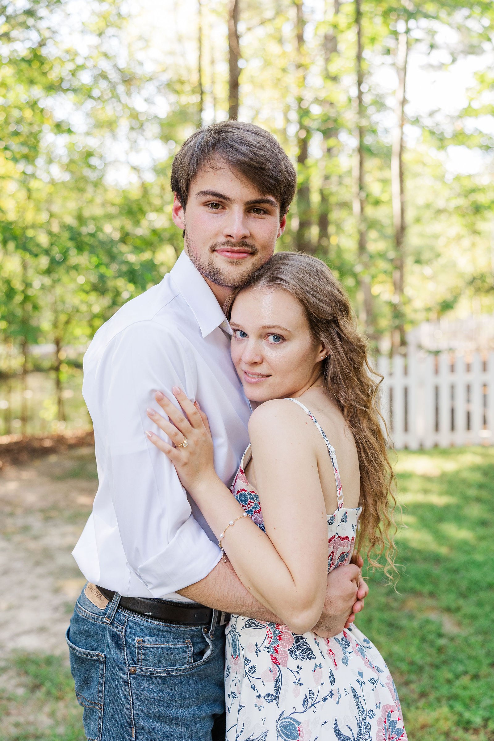 Dylan holds Emma beside a white picket fence during their Shiloh Gardens engagement photos in Cumming, GA