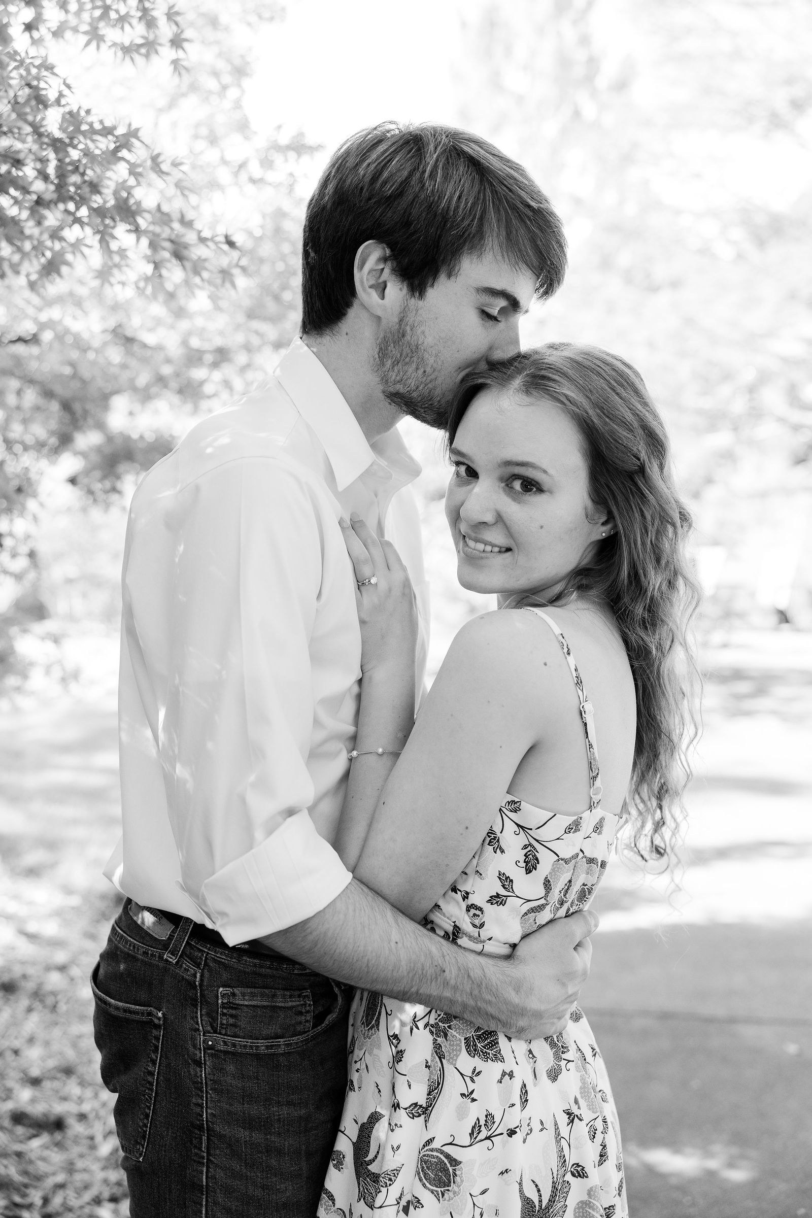 Black and white engagement photo of Dylan kissing Emma's forehead